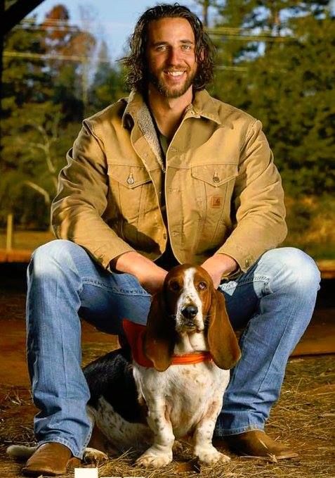 a man sitting on the ground next to a brown and white basset hound dog