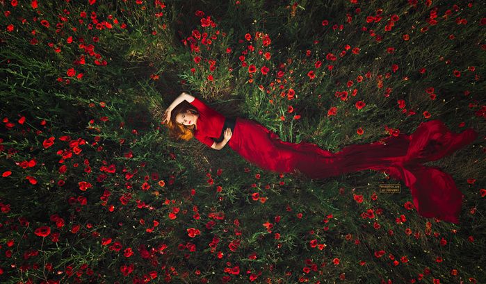 a woman laying in the middle of a field of flowers wearing a red dress and hat