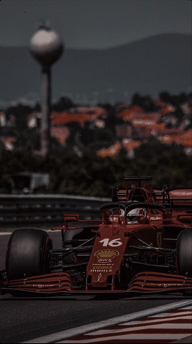 a red race car driving on a track with the city skyline in the back ground