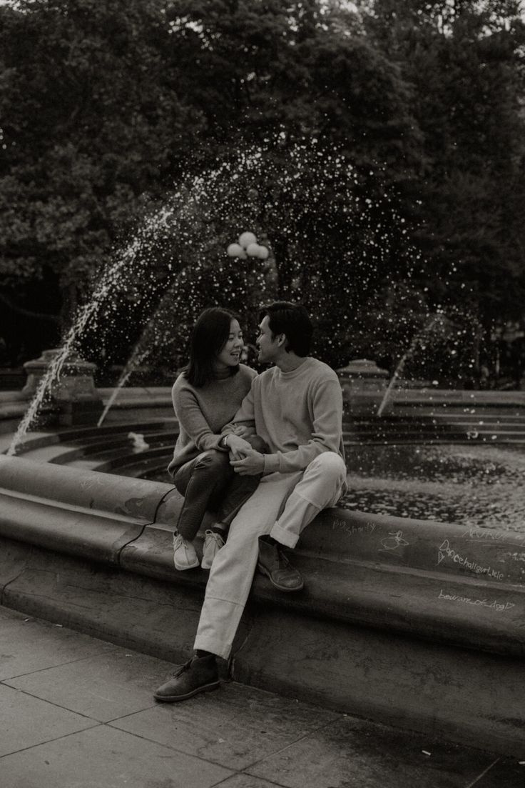 a man and woman sitting next to each other on a fountain with water shooting from it