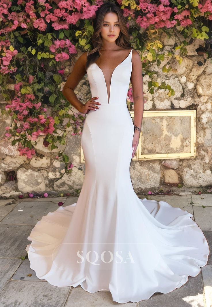 a woman in a white wedding dress standing next to a stone wall with pink flowers