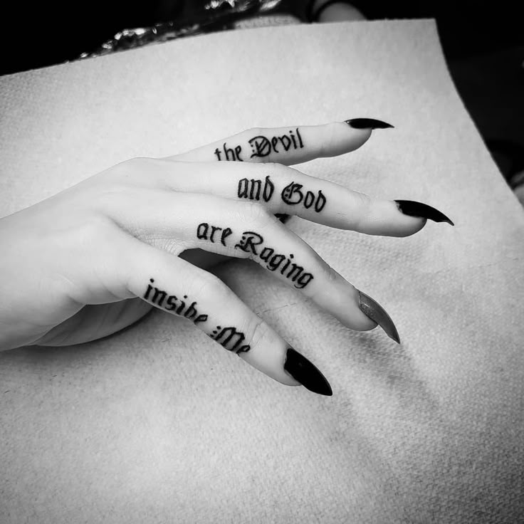 two hands with black and white nail polish on them, one has the words in gothic script