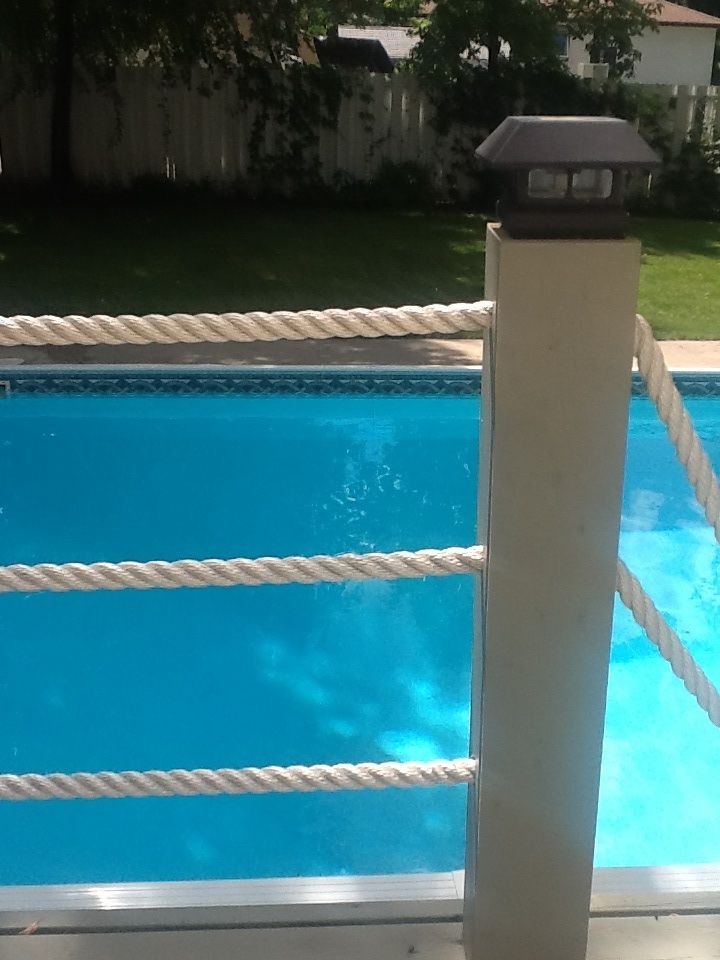 an empty swimming pool next to a white rope fence with a clock on it's post