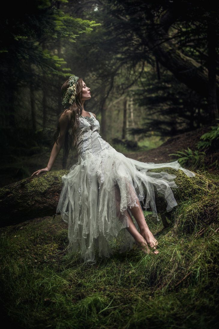 a woman in a white dress sitting on top of a lush green forest covered in grass