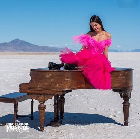 a woman in a pink dress sitting on top of a piano