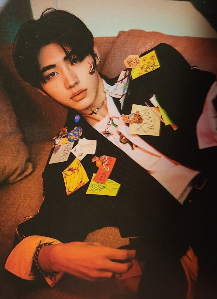 a young man sitting on top of a couch wearing a jacket with many stickers all over it