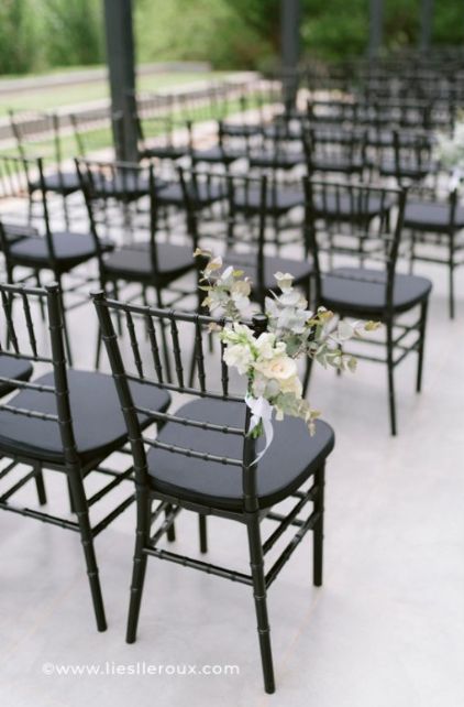 rows of black chairs with white flowers and greenery on them for an outdoor ceremony