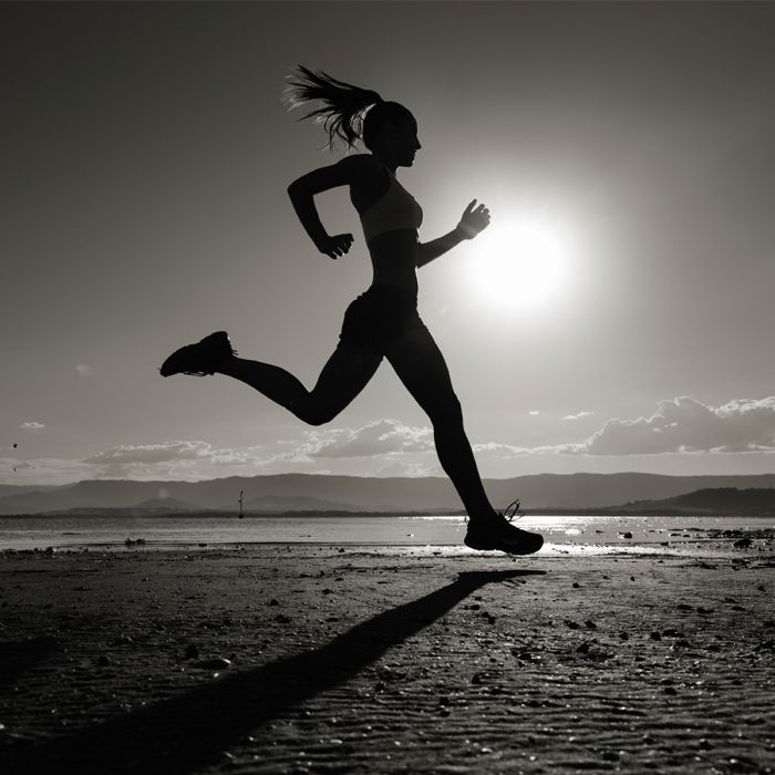 a woman is running on the beach in front of the sun with her hair blowing in the wind