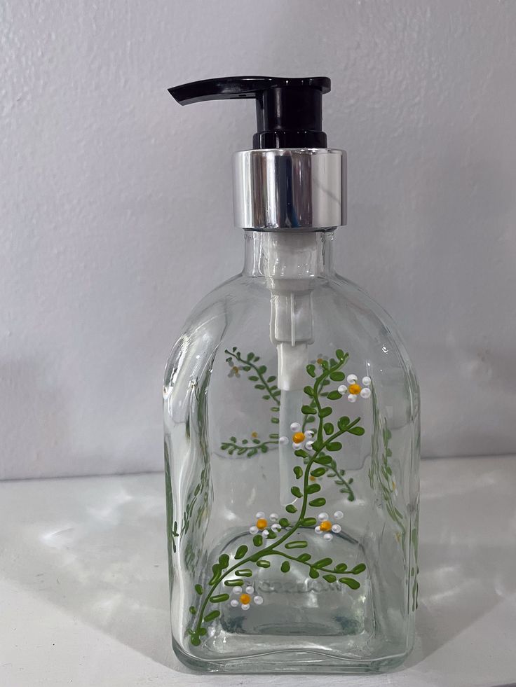 a glass soap dispenser with flowers painted on the front and bottom, sitting on a white surface