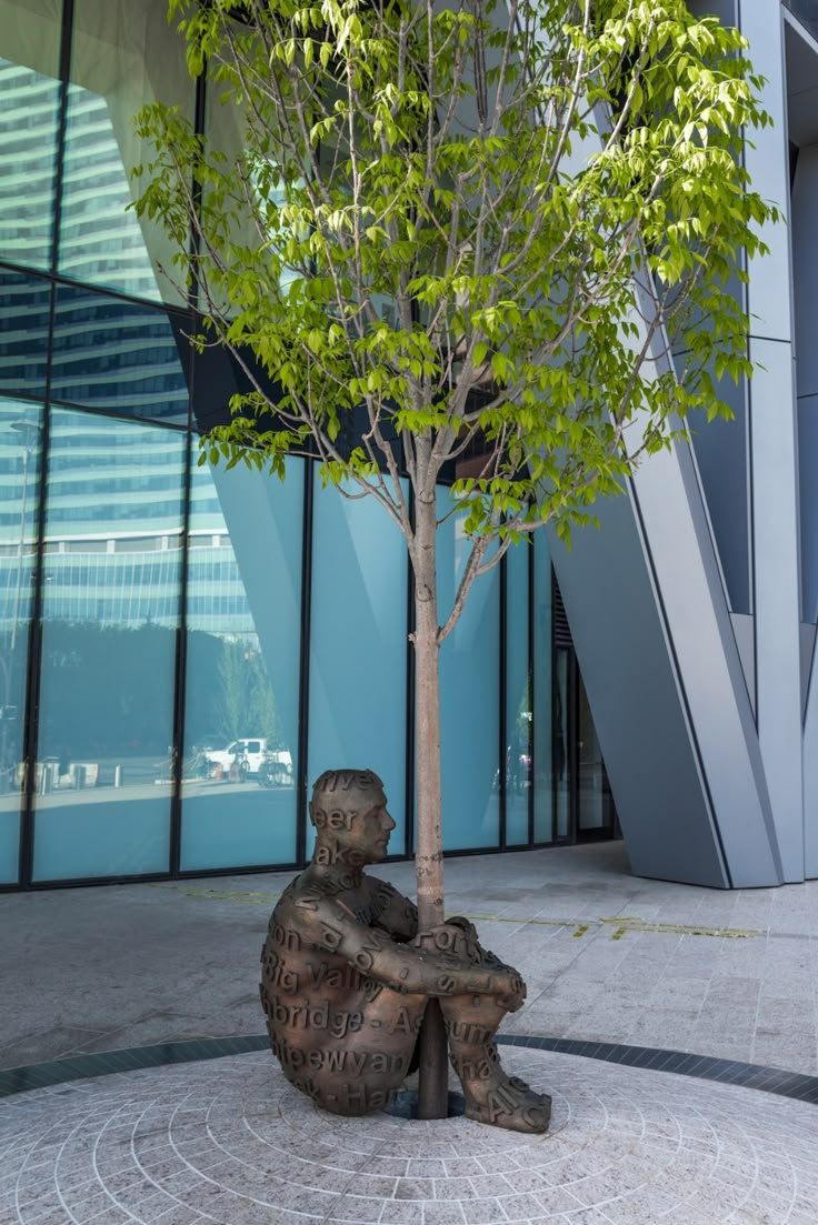 a statue sitting under a tree in front of a building with glass walls and windows