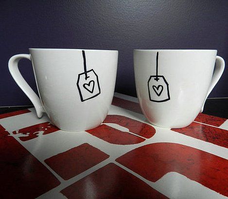 two coffee mugs with tags on them sitting next to each other in front of a wall