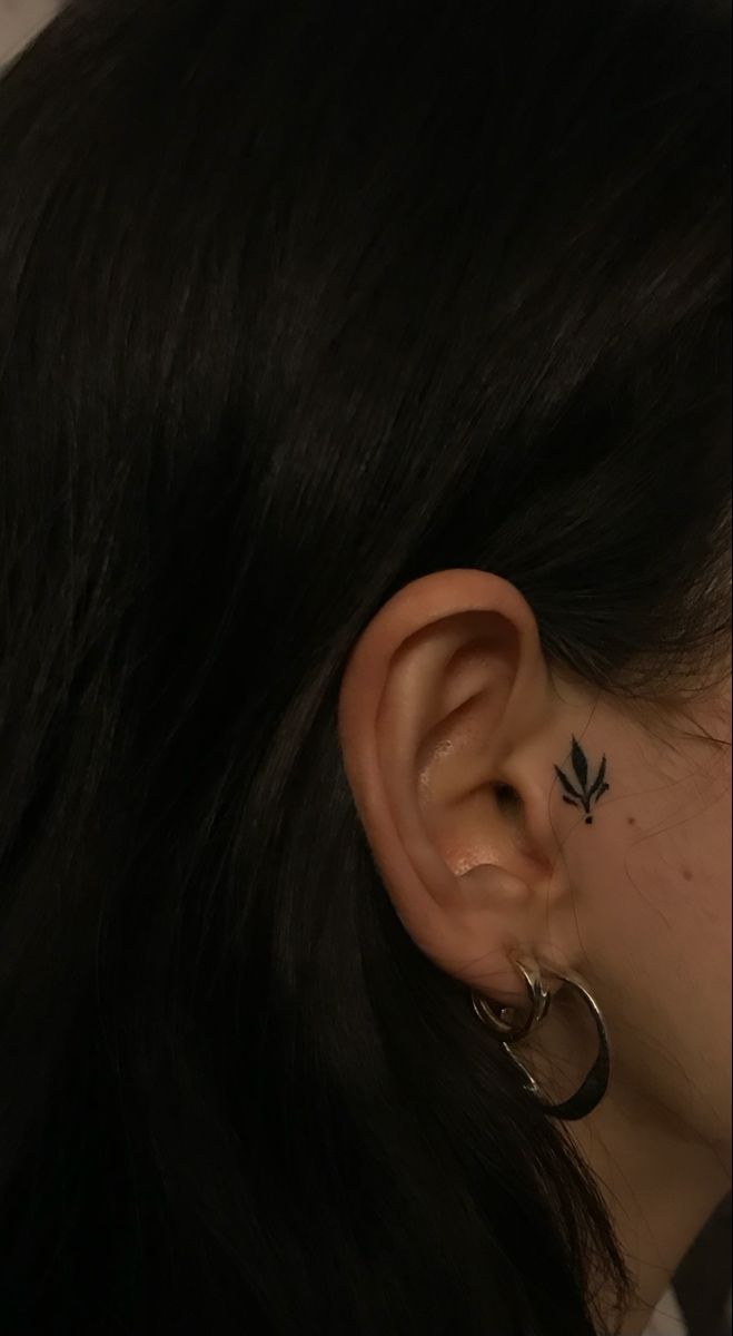 a woman's ear with a small leaf tattoo on the left side of her ear