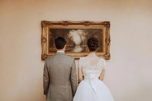 a bride and groom standing in front of a painting