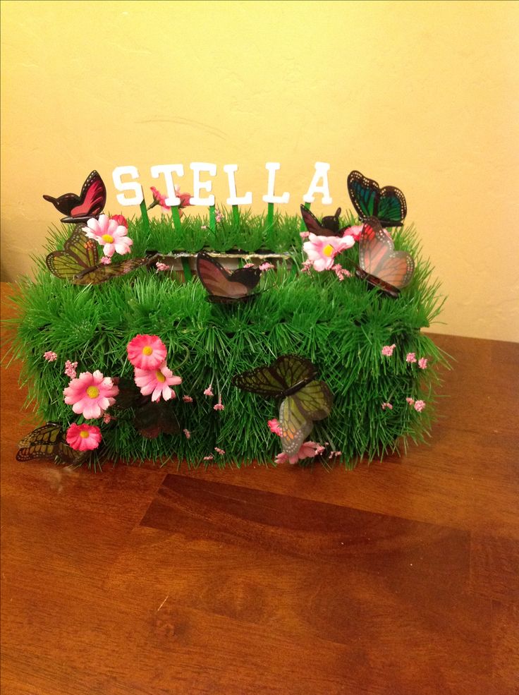 a wooden table topped with green grass covered in flowers and butterflies next to a sign that says stella