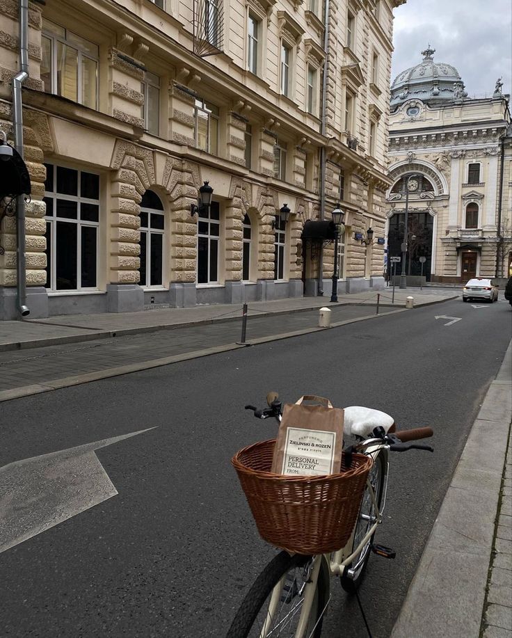 a bicycle with a basket parked on the side of an empty street in front of a building