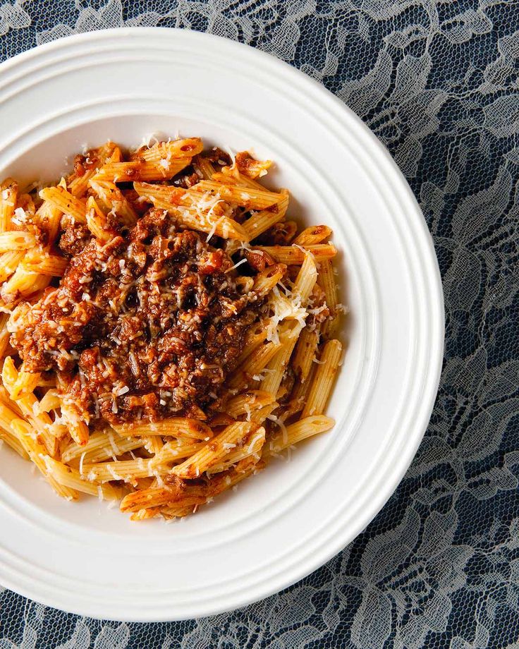 a white plate topped with pasta covered in meat and sauce on top of a table