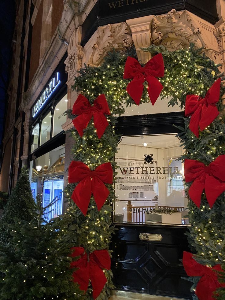 christmas wreath with red bows and lights in front of a department storefront at night