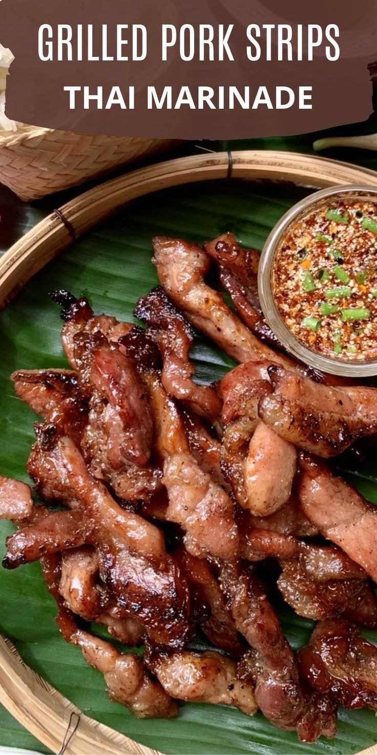 grilled pork strips on a banana leaf with dipping sauce