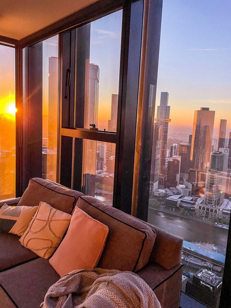 a living room filled with furniture next to a window overlooking a cityscape at sunset