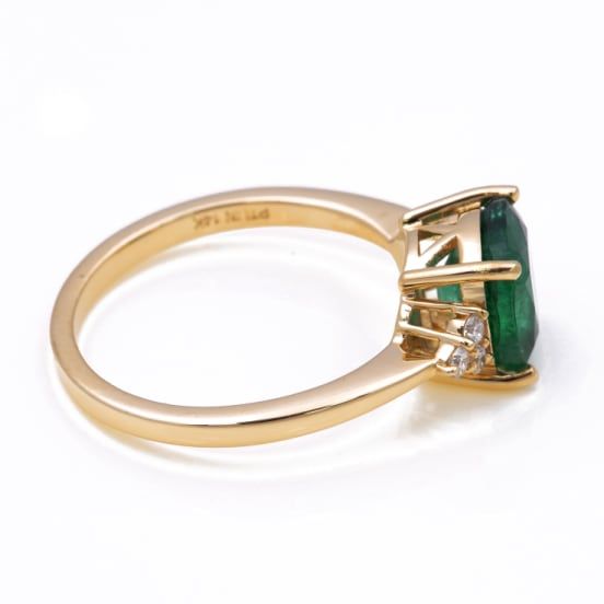 an emerald and diamond ring on a white background, with the top stone in yellow gold