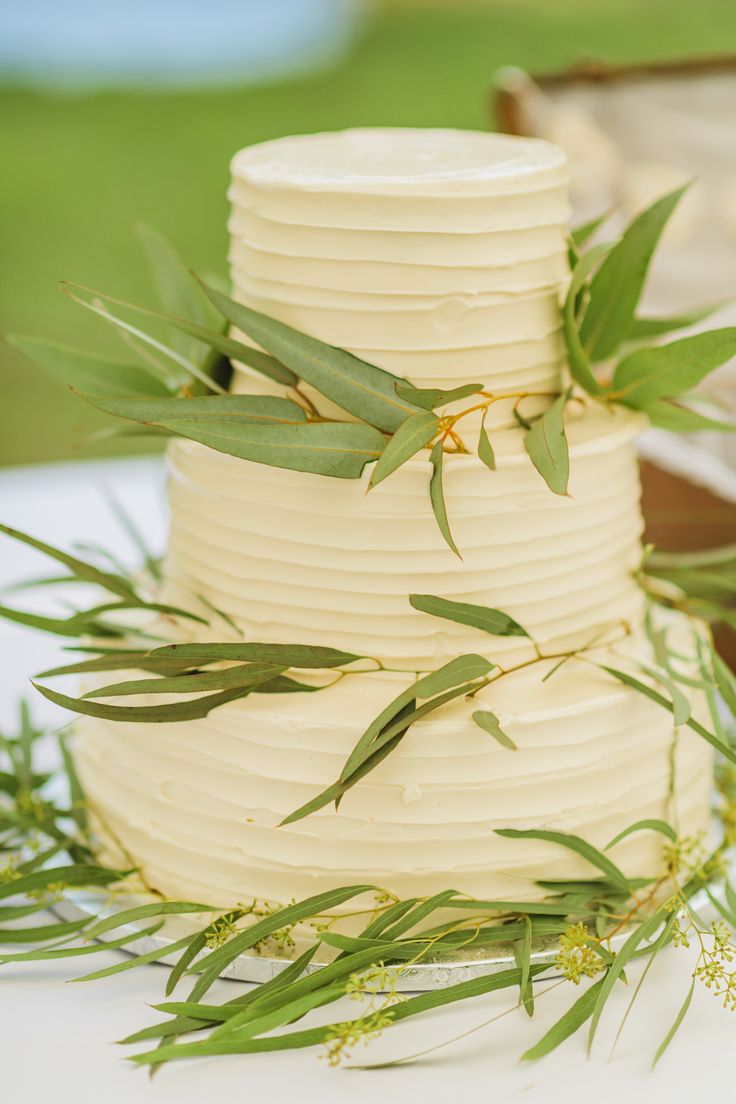 a three tiered white cake with green leaves on top