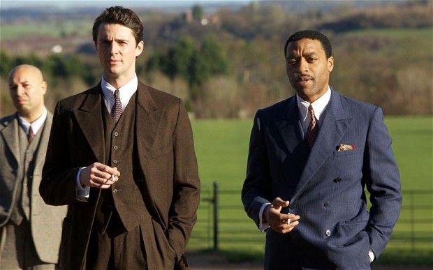 three men in suits standing next to each other near a fence and grassy area with trees