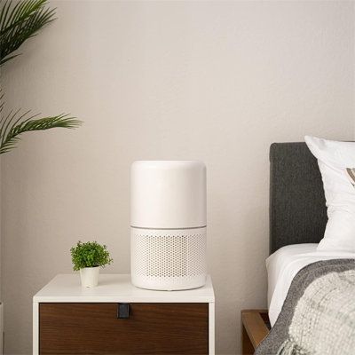 a white air purifier sitting on top of a nightstand next to a bed