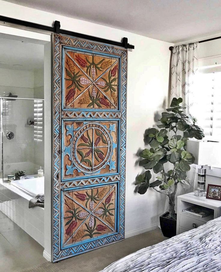 a bedroom with a bed, bathtub and large door to the shower area that has an intricately painted design on it