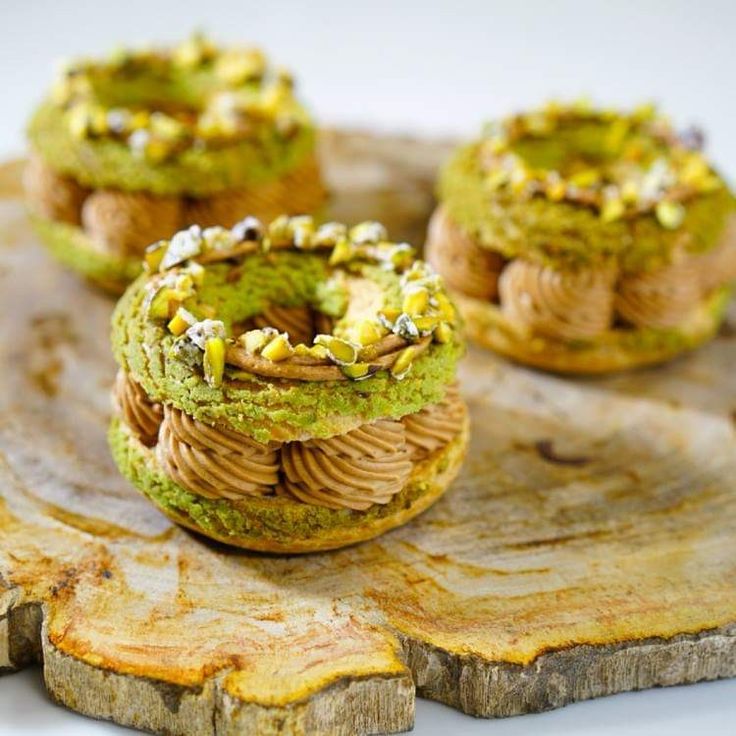 three pastries with green and yellow toppings on a wooden platter