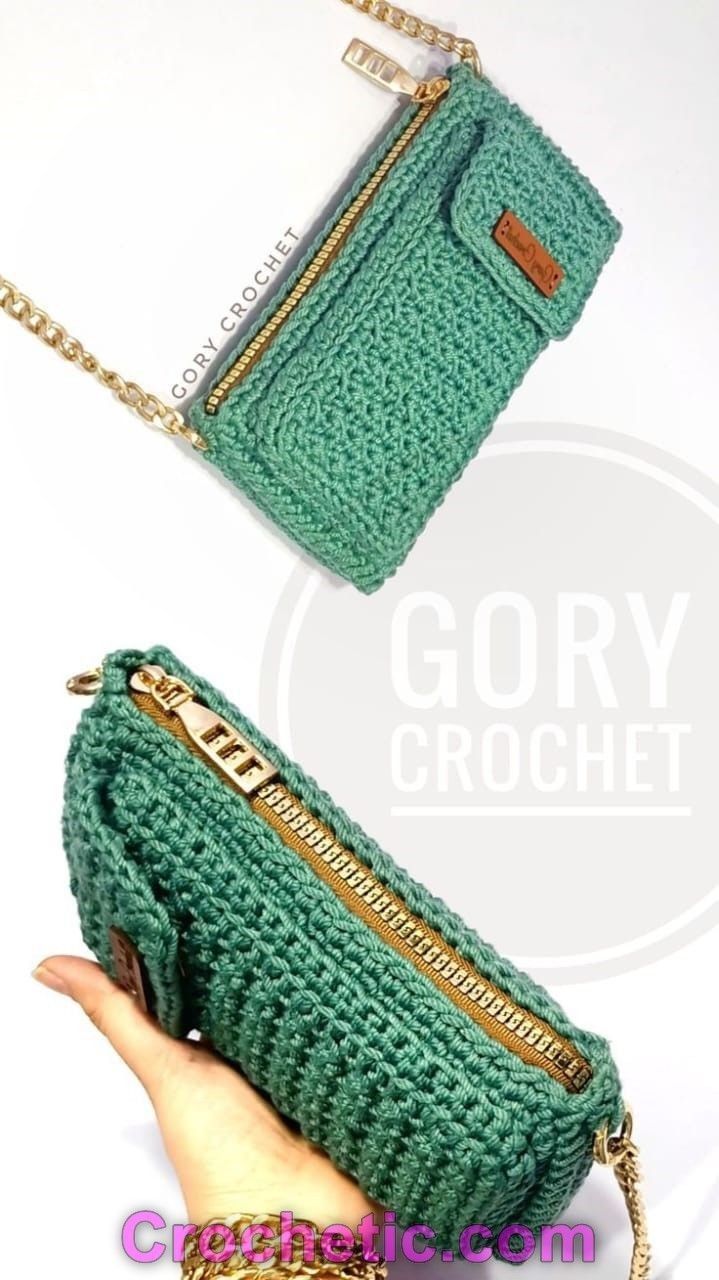 a hand holding a green crocheted purse with gold zippers on the front and side