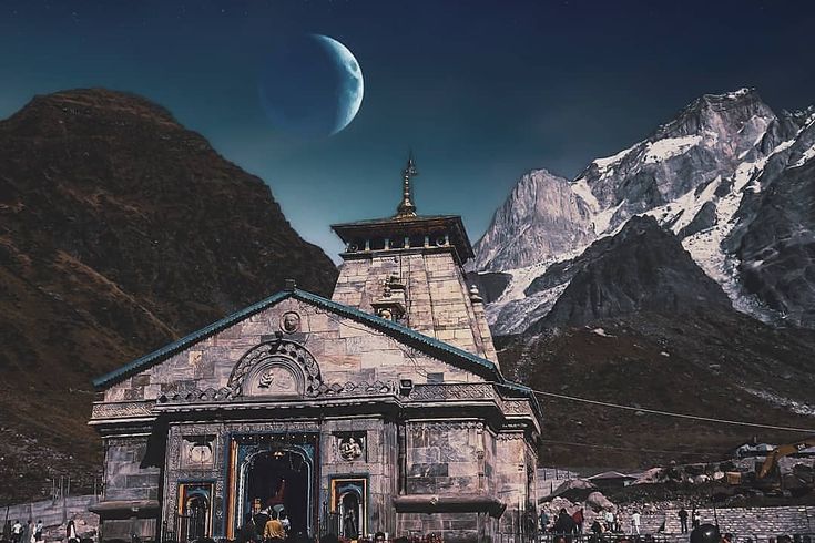 an old church with mountains in the background and a half moon rising over it's top