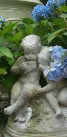 there is a statue of two children holding each other in front of some blue flowers