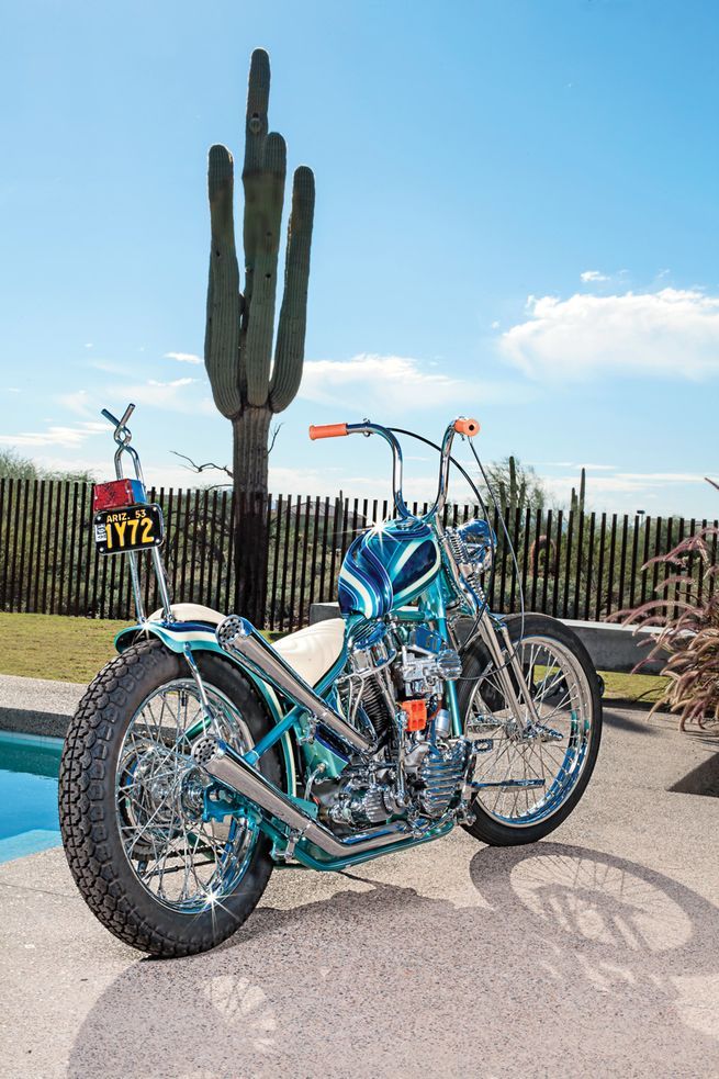 a blue motorcycle parked next to a tall cactus in front of a fenced pool