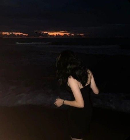 a woman is standing on the beach at night with her back to the camera, facing the water