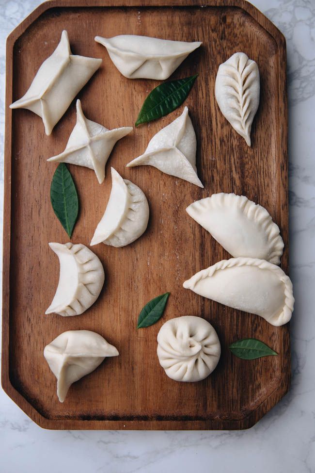 some dumplings are on a wooden tray with green leaves