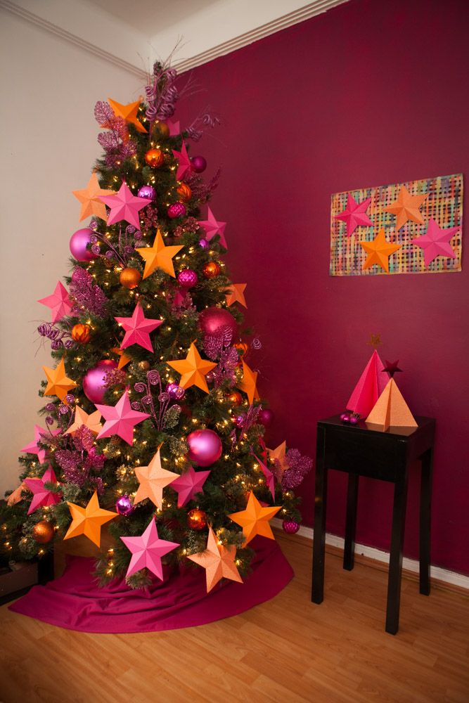 a decorated christmas tree with pink and orange stars in the center, against a red wall