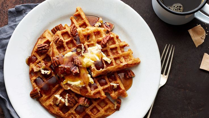 a waffle topped with butter and nuts on a white plate next to a cup of coffee