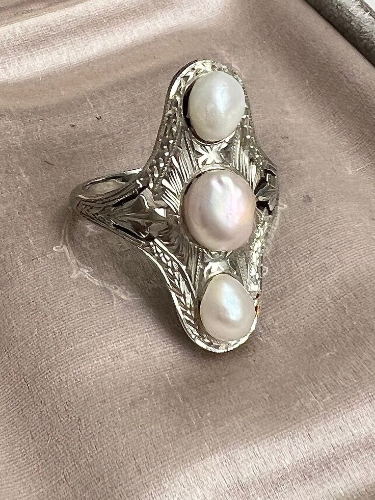 "For your consideration this Early Art Deco dinner ring. Skillfully crafted in solid white 14k gold and meticulously covered with hand engraving. The setting is all hand chased and hand pierced. Beautifully decorated with three hard to find natural pearls of cream and cream-rose colors.  The ring is \"a true antique\" and was crafted 1920-s circa, not a modern reproduction. In very good estate found condition with some surface wear from age/being worn.  Currently offered in size 7 Total weight 6 Silver Rings With Historical Design As Gift, Silver Rings With Historical Design For Gifts, Oval Heirloom Pearl Ring, Silver Heirloom Jewelry With Historical Design, Vintage Pearl Ring With Gemstone, Heirloom Silver Jewelry With Historical Design, Victorian Engraved White Gold Filigree Ring, Antique White Gold Pearl Ring For Wedding, Antique Pearl Ring With Gemstone For Anniversary