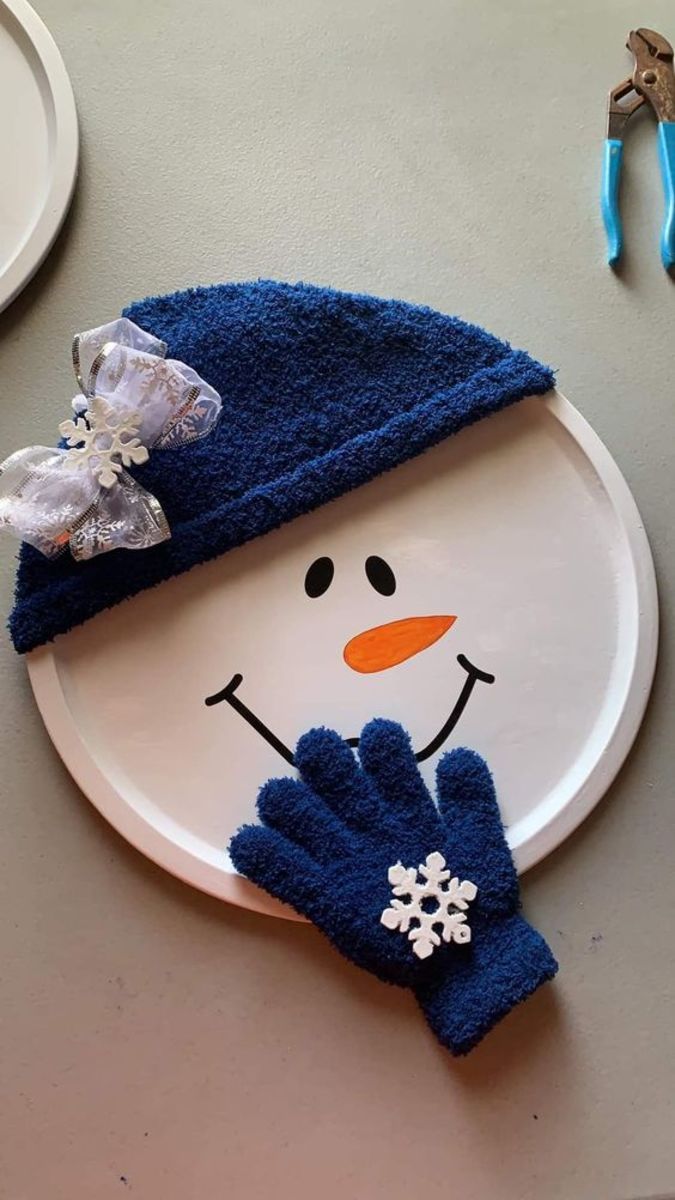 a paper plate with a snowman face on it and blue mittens around the edge