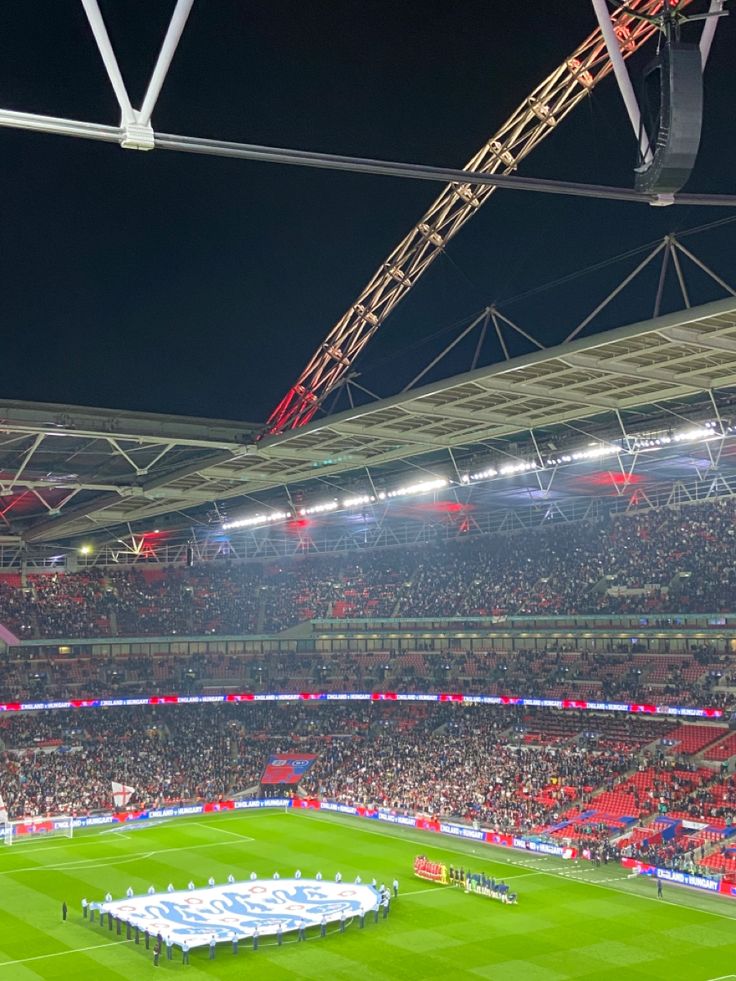 a stadium filled with lots of people watching a soccer game on the field at night