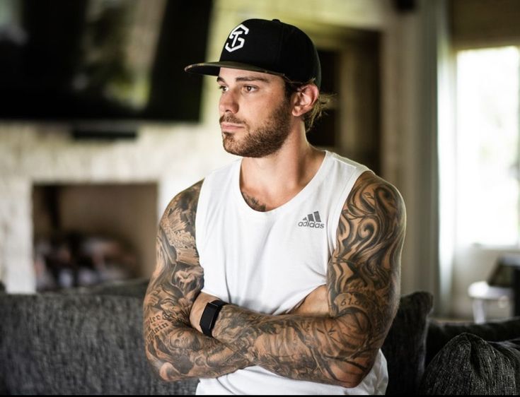 a man with his arms crossed sitting on a couch wearing a black and white hat