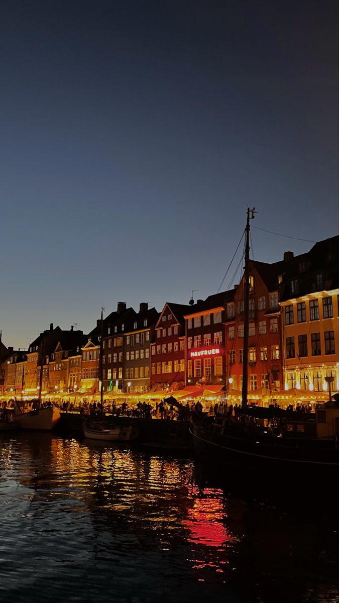 boats are docked in the water next to some buildings at night with lights on them