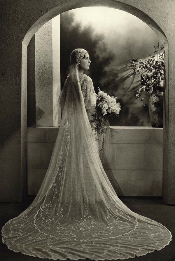 an old black and white photo of a woman in a wedding dress looking out the window