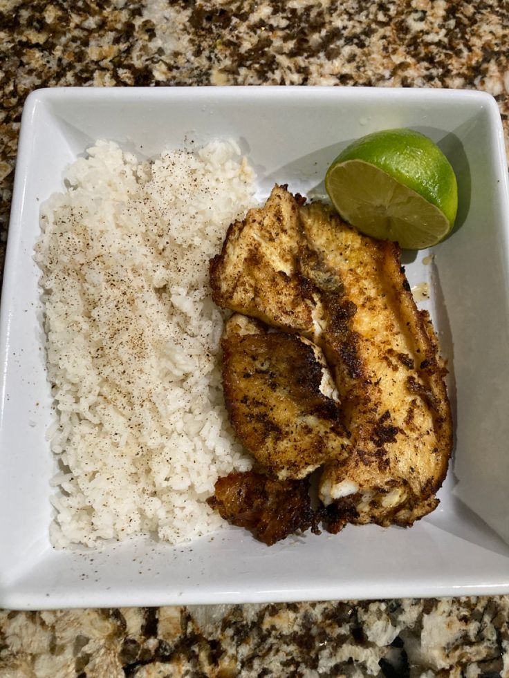 a white plate topped with rice and chicken next to a lime wedge on top of a counter