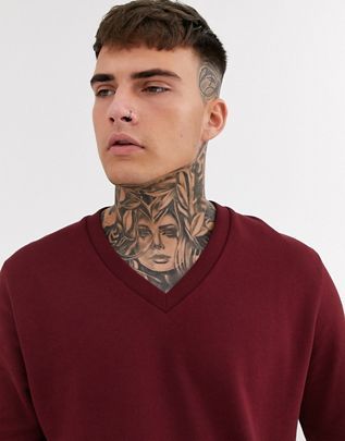 a man with tattoos wearing a red v - neck sweater