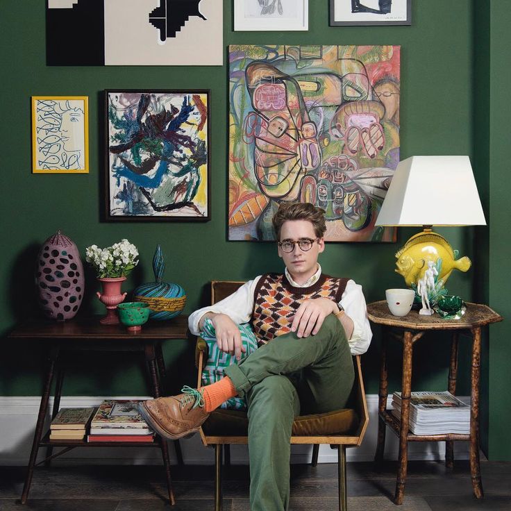 a man sitting in a chair next to a table with pictures on the wall behind him