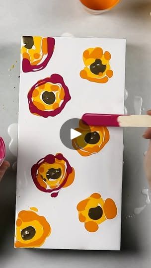 someone is painting an orange and red flower on a piece of paper with a brush