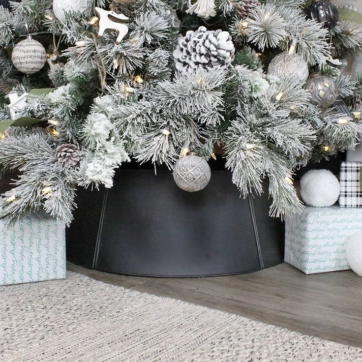 a christmas tree in a black pot with silver ornaments and pine cones on the top