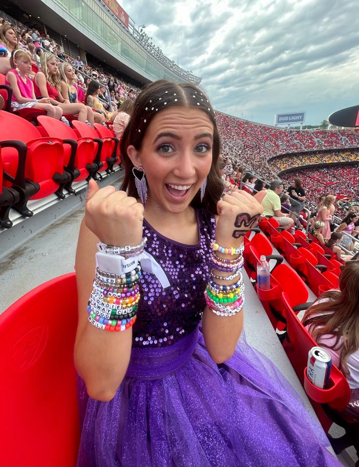 a woman in a purple dress sitting on a red chair at a baseball game wearing bracelets