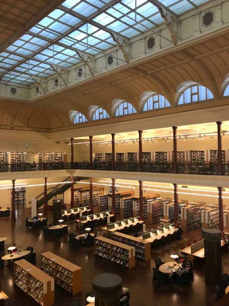 the interior of a large library with lots of books on shelves and tables in it